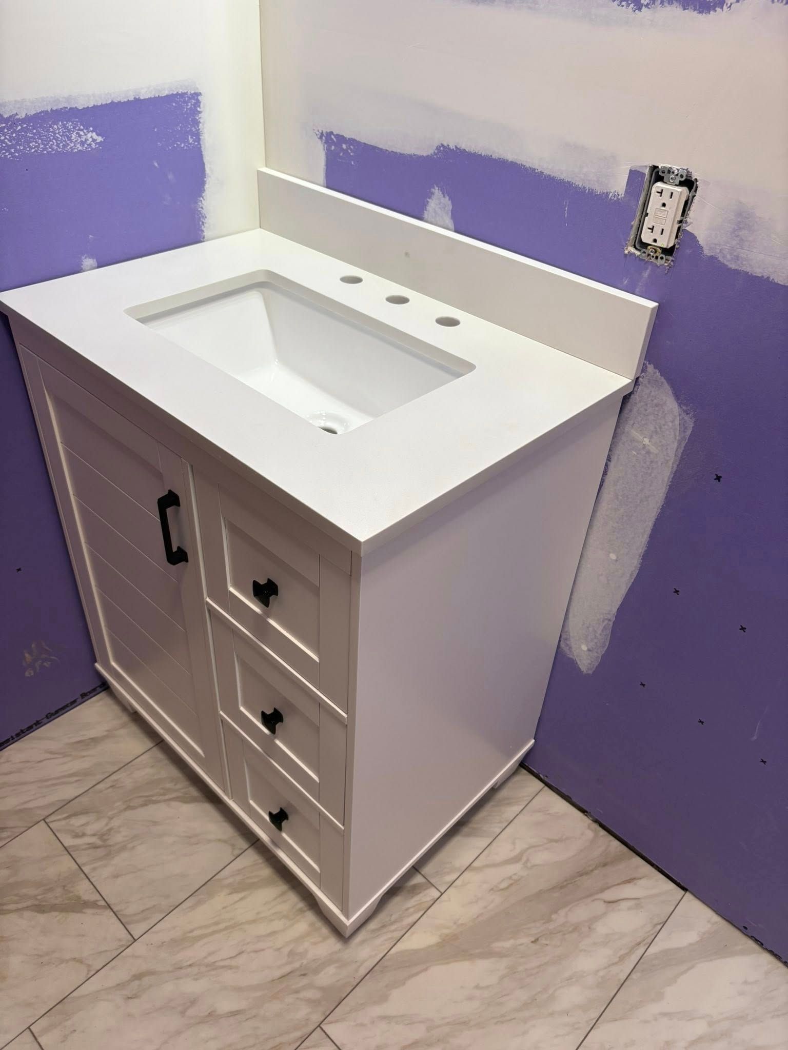 White bathroom vanity with sink and countertop, installed against purple drywall, and beige tiled floor.
