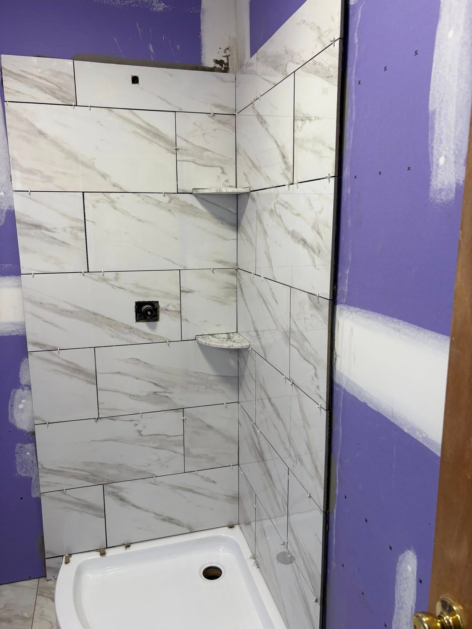 Shower with white marble-look tiles partially installed; purple drywall surrounds the tiled area.
