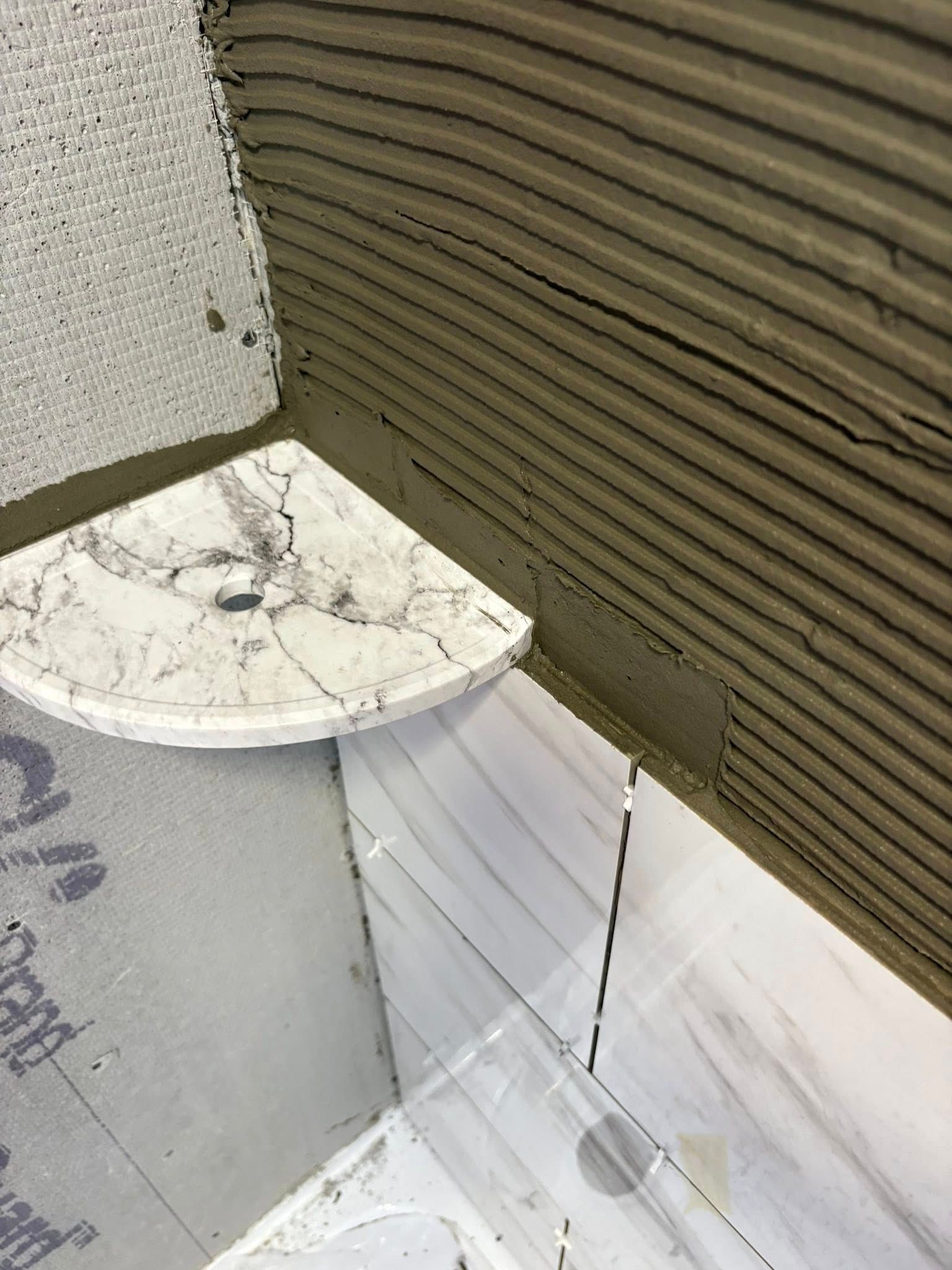 Corner tile installation, corner shelf in place, mortar spread.
