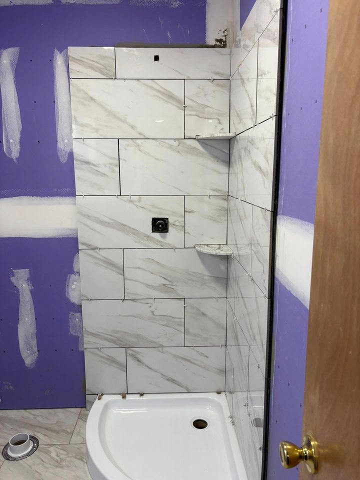 Shower under construction with tiled walls, shelves, and a white shower basin. Drywall is visible.