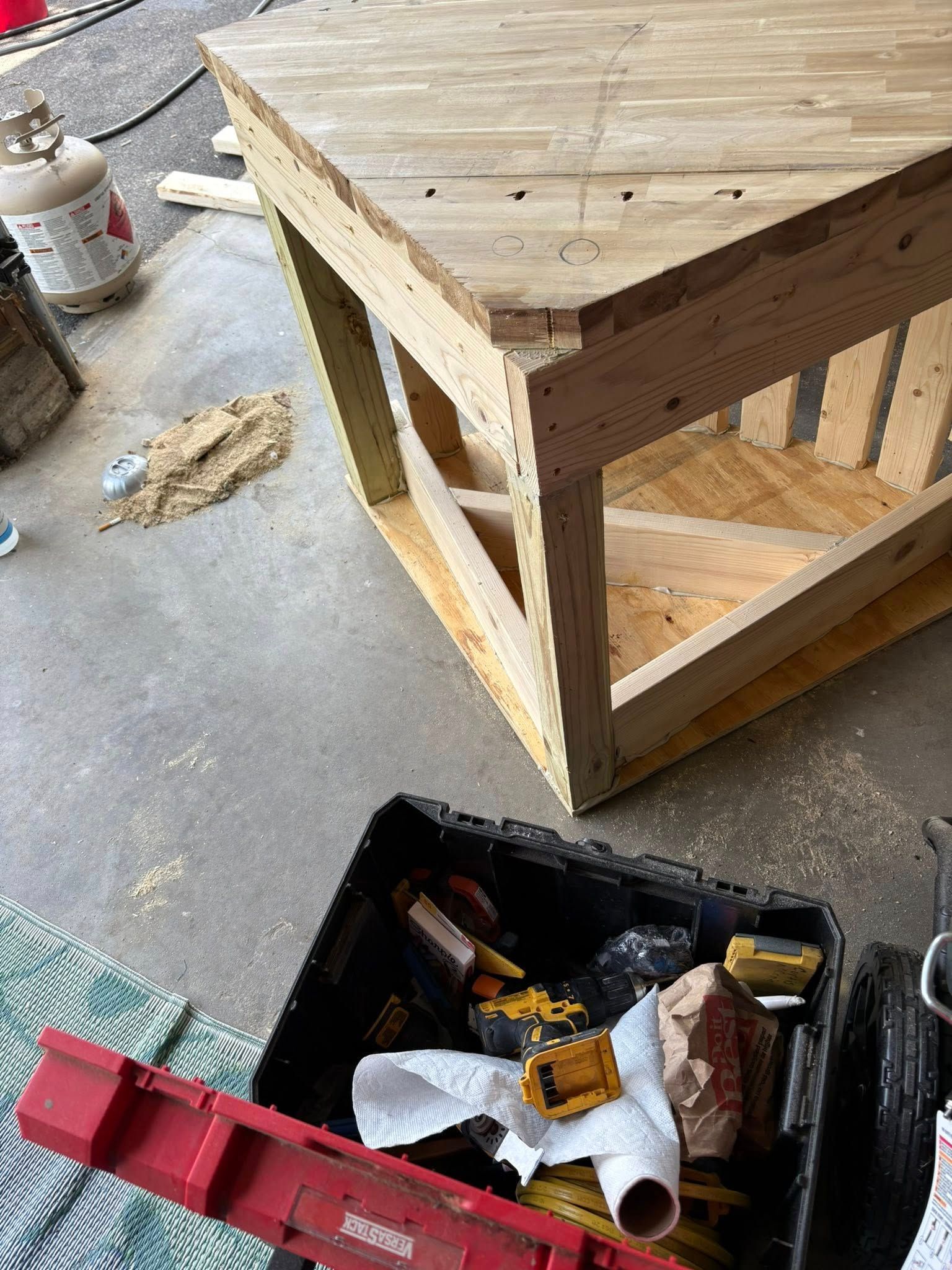 Wooden triangular table being constructed outdoors, tools and materials scattered nearby.
