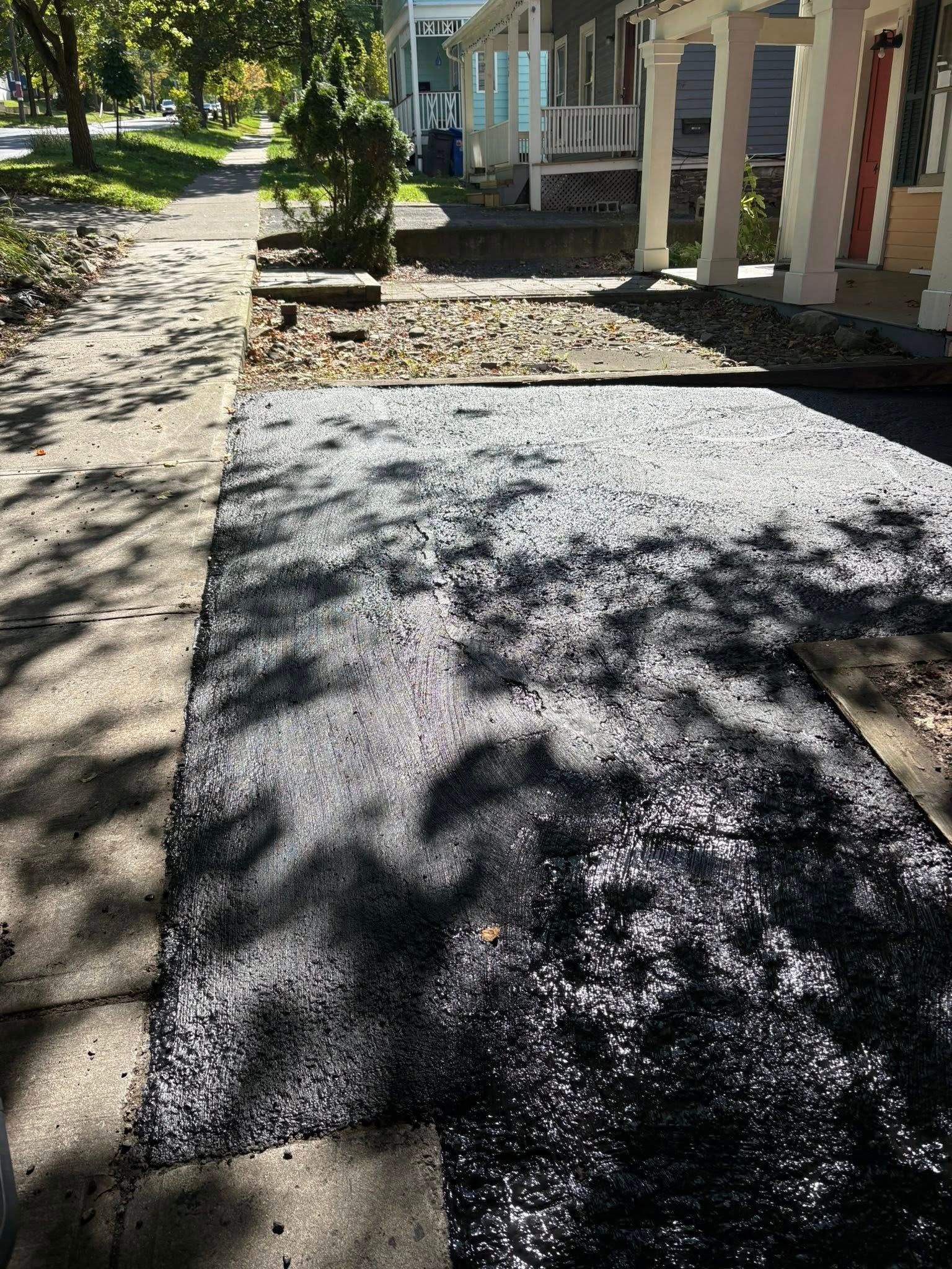 Freshly paved driveway with a sidewalk and houses in the background on a sunny day.