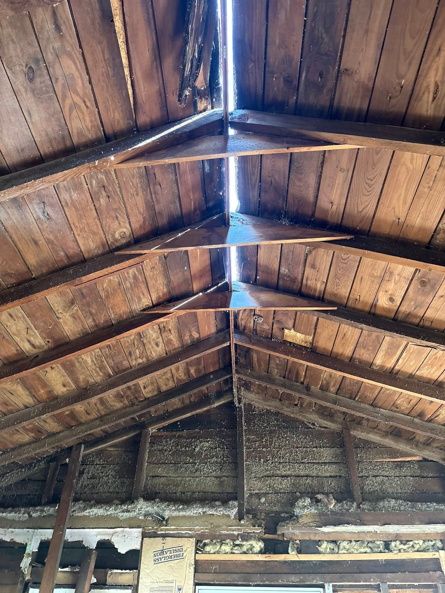Inside of an old wooden roof with visible rafters and light shining through a gap.