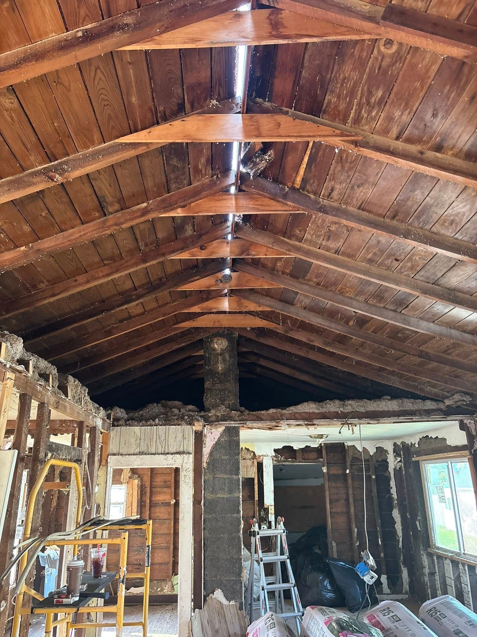 Interior of a home under renovation, showing exposed rafters, damaged walls, and construction debris.