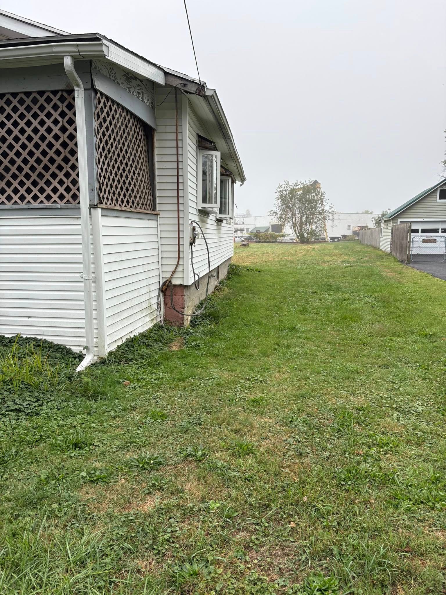 White house with porch and sloped lawn.  Garage visible in the distance; cloudy sky.