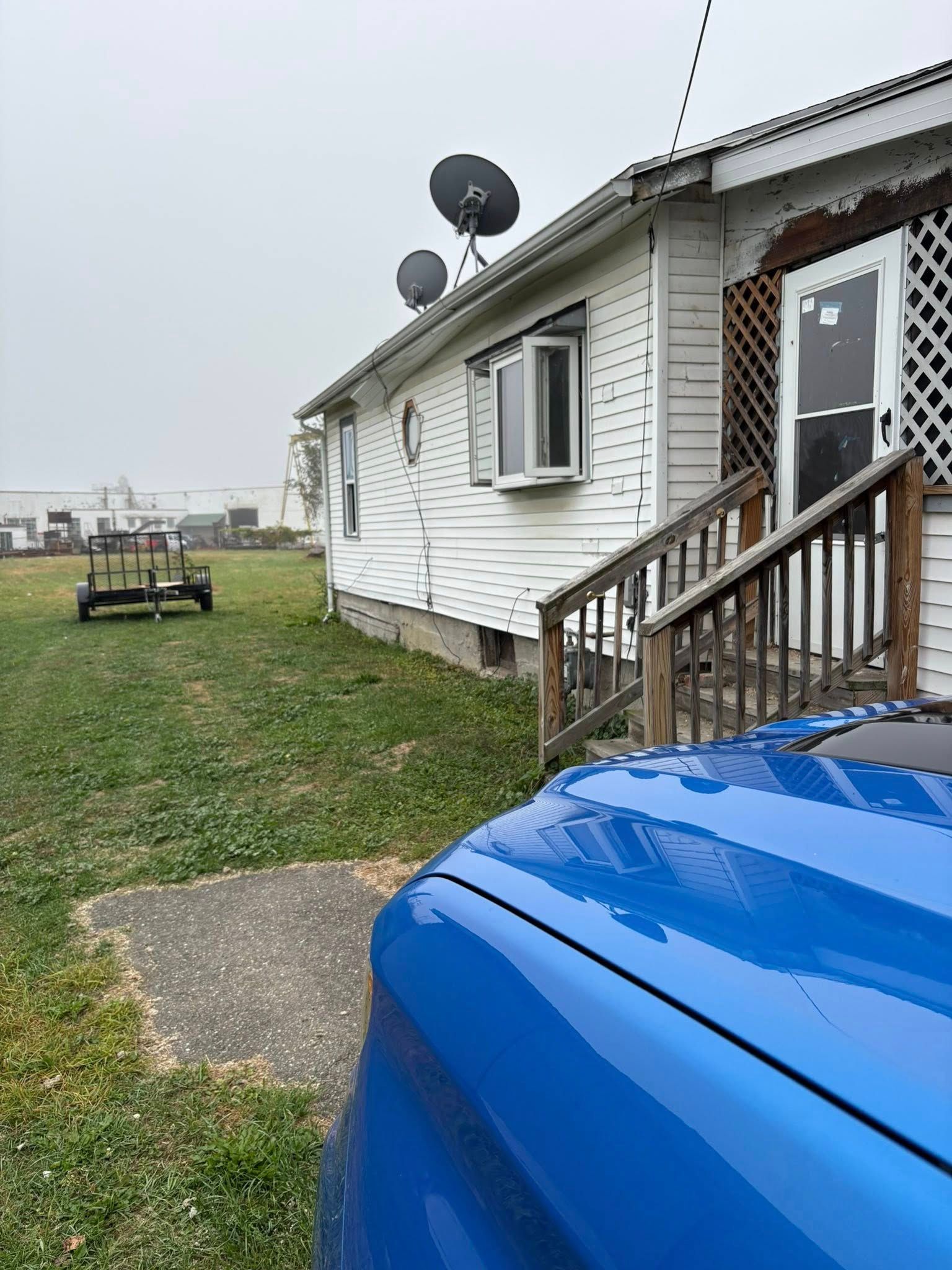 Blue car parked near a white house with satellite dishes. Overcast day.