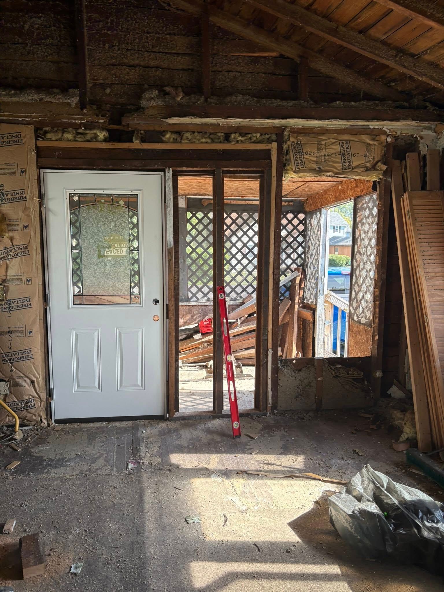 Interior view of a room under renovation, with a white door, lattice divider, and exposed wooden structure.