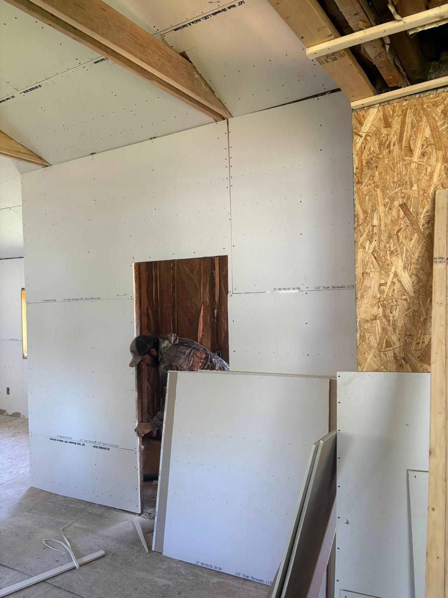 Interior construction site with drywall installed on walls, exposed beams, and open doorway.