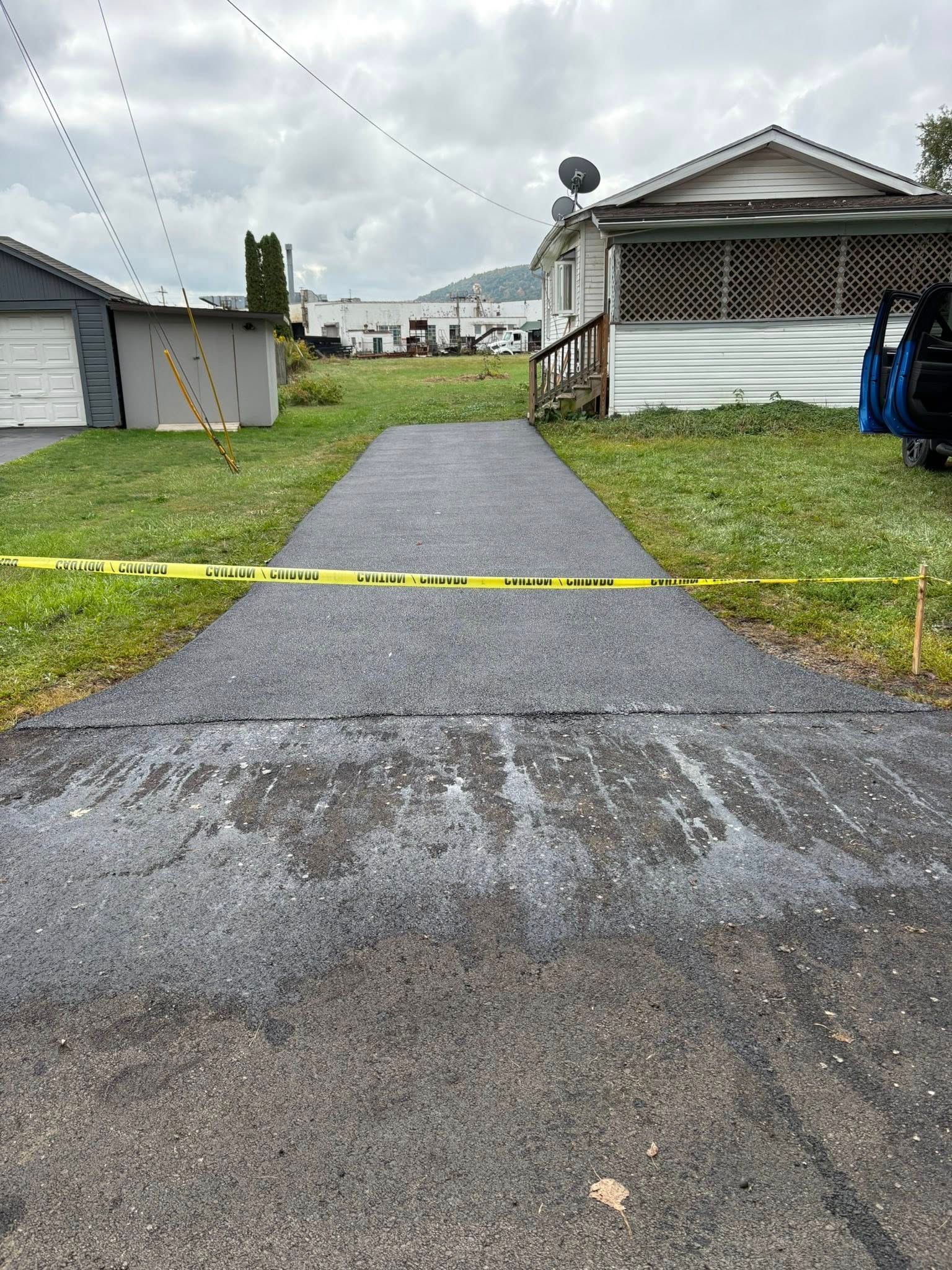 Driveway blocked by yellow caution tape; houses and cloudy sky in background.