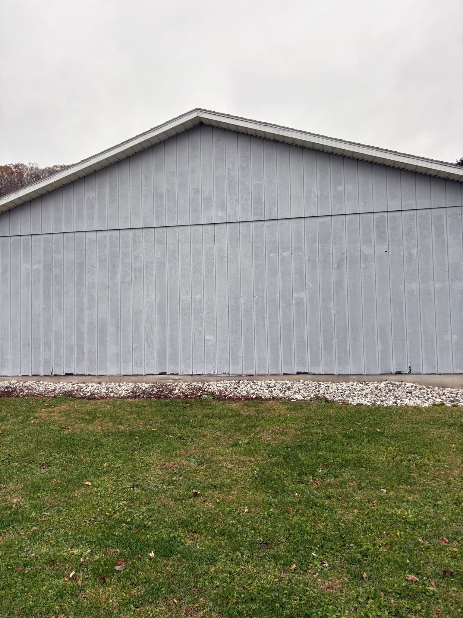 Gray-sided building with white trim, set on green grass and gravel under an overcast sky.