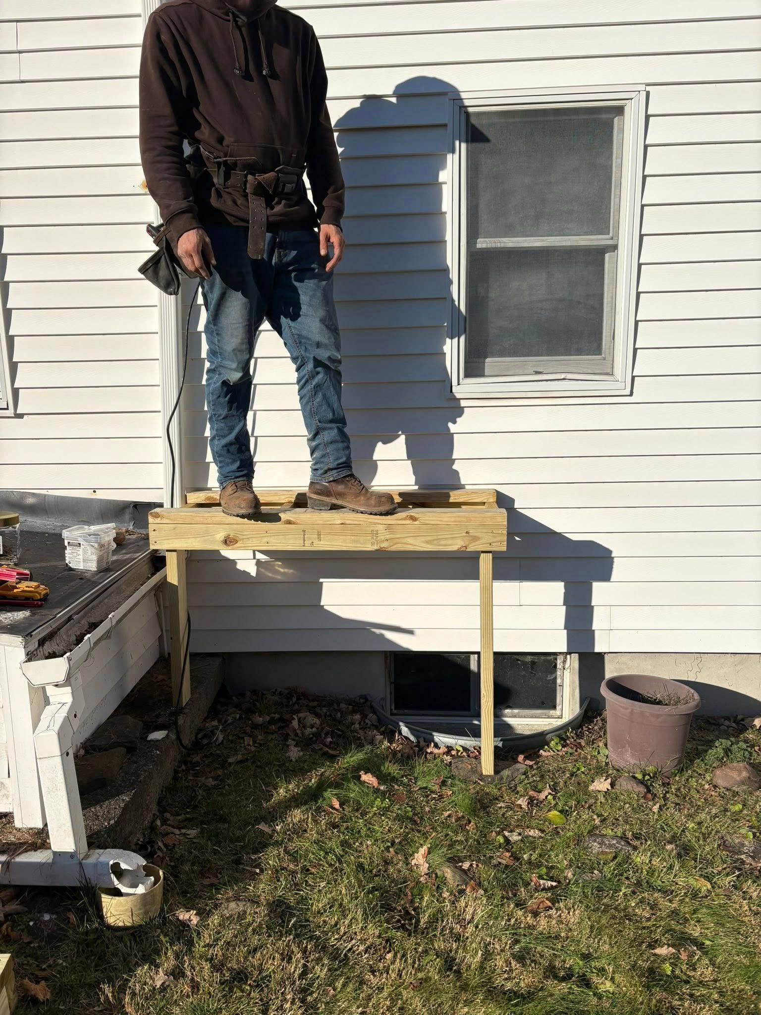 Person standing on a small wooden platform in front of a house.