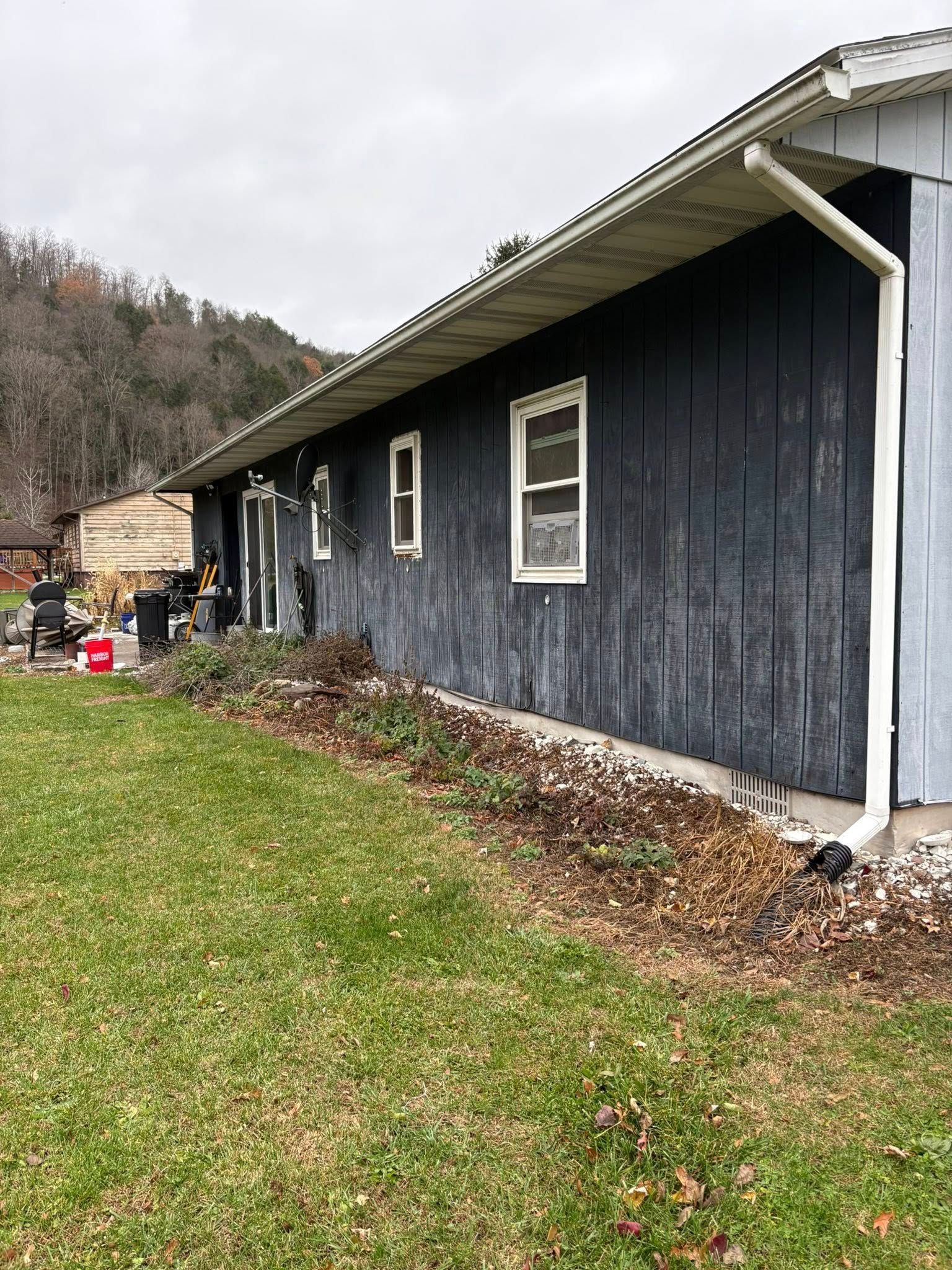 Dark blue house with white trim and a green lawn, beside a hillside.