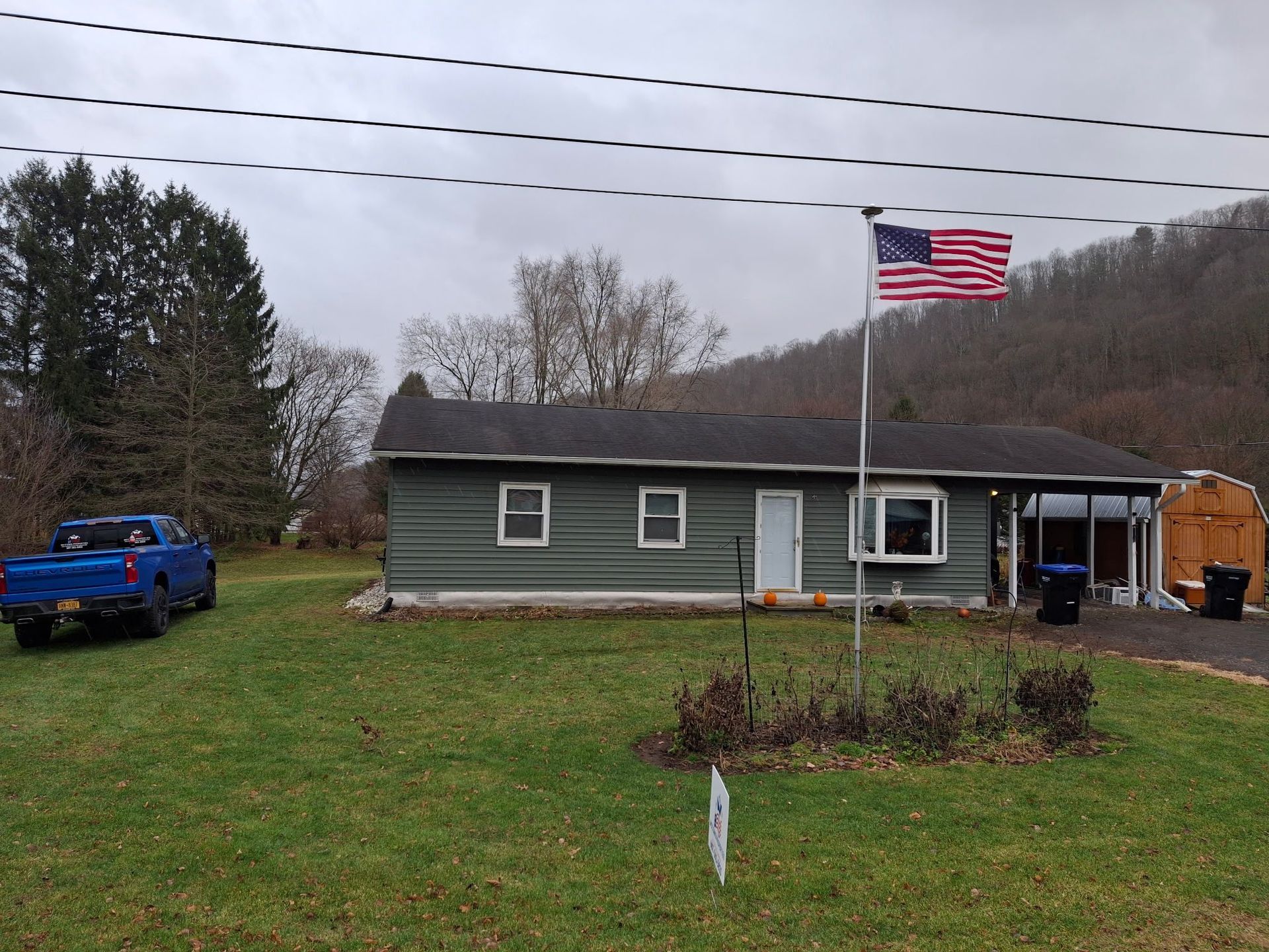 Green house with American flag, blue truck, and cloudy sky in a grassy yard.