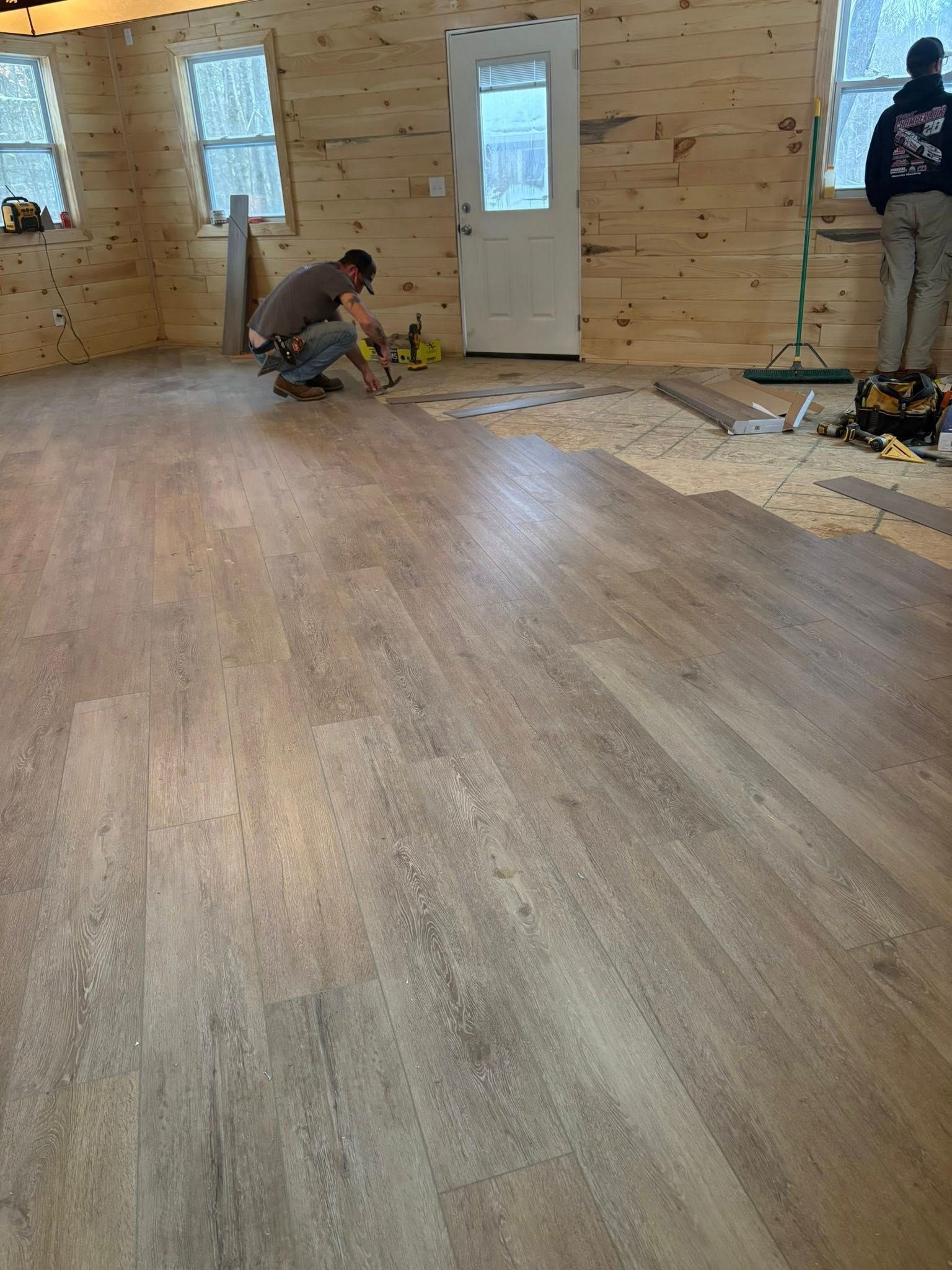 People installing new wood flooring in a room with wood walls.