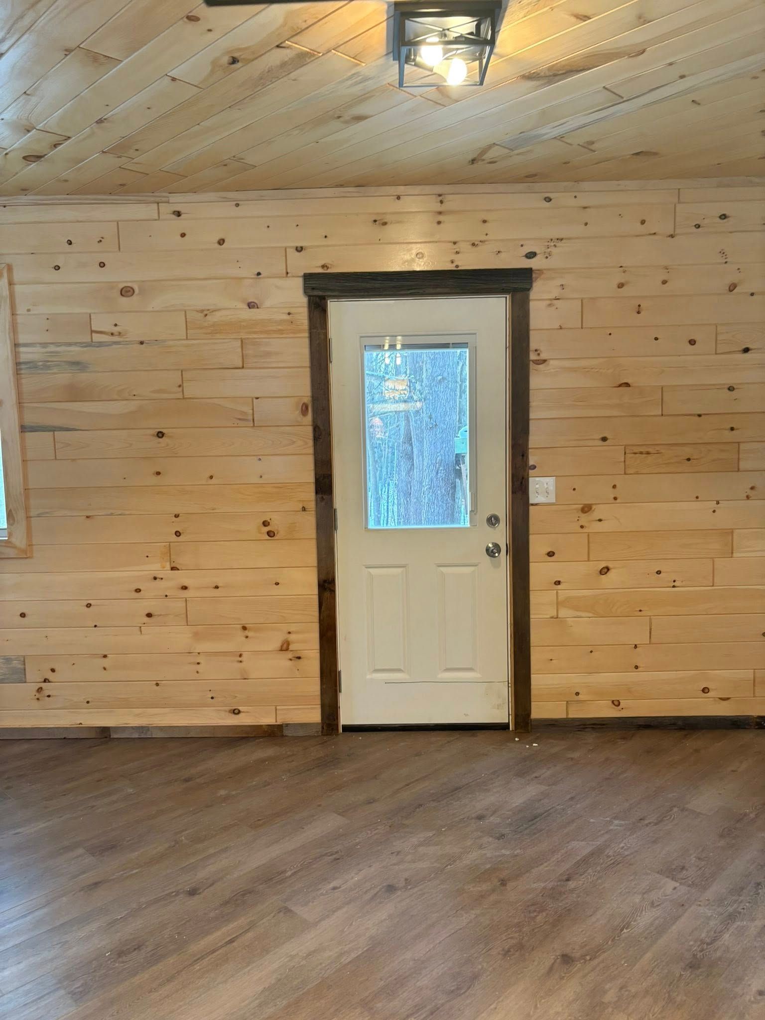 Interior of a room with wood-paneled walls and ceiling, white door, and laminate flooring.