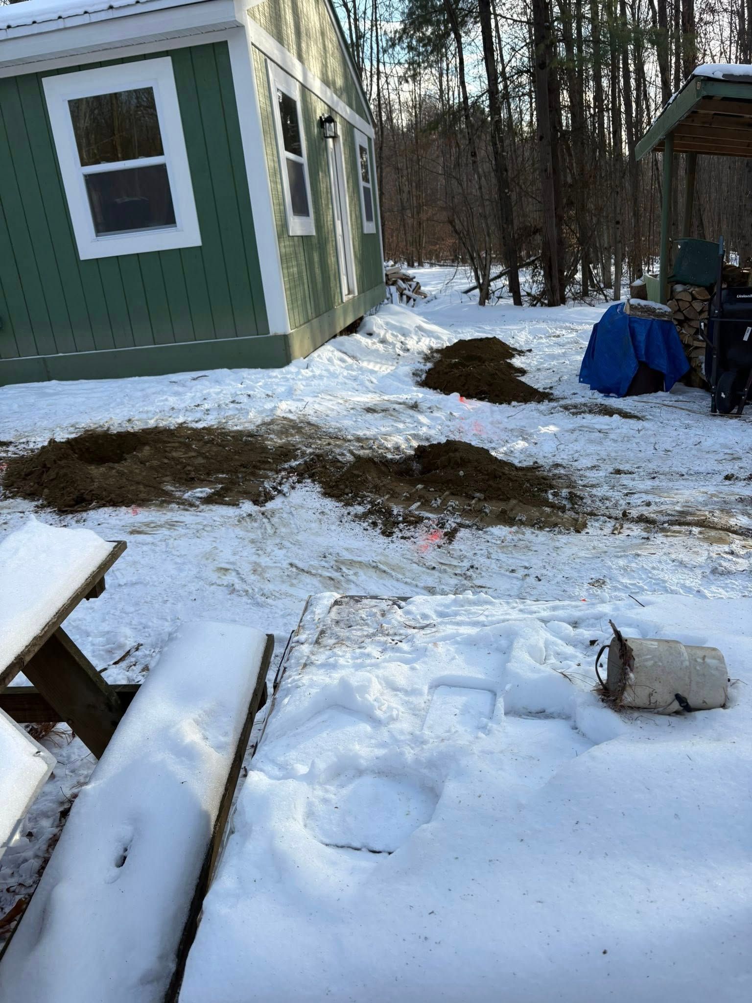 Snowy yard with green shed, piles of dirt, and a picnic table.