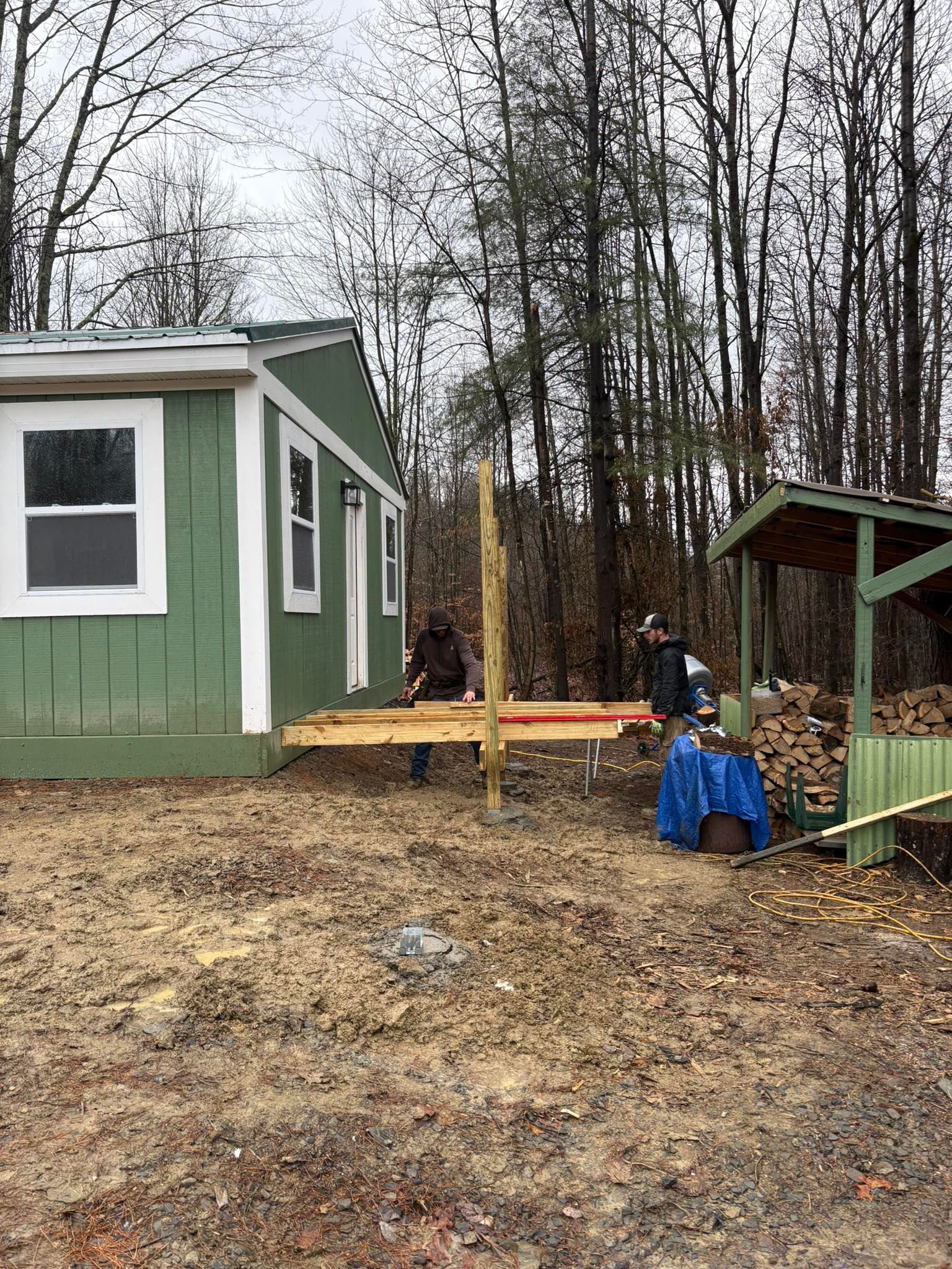 Construction workers building a wooden deck next to a green building in a wooded area.