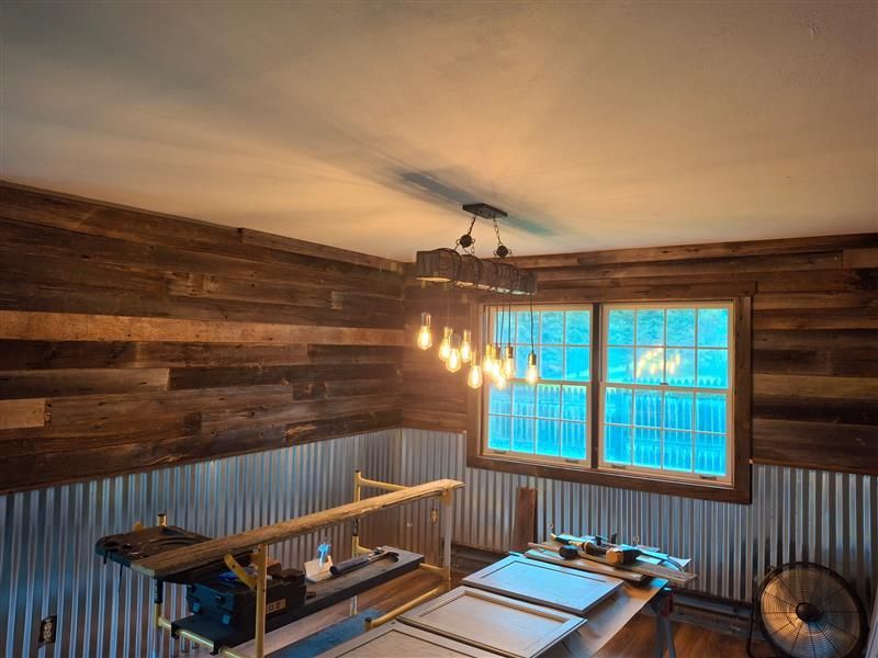 Rustic-style room with wood panel walls, corrugated metal, and a window. A work table and light fixture are visible.