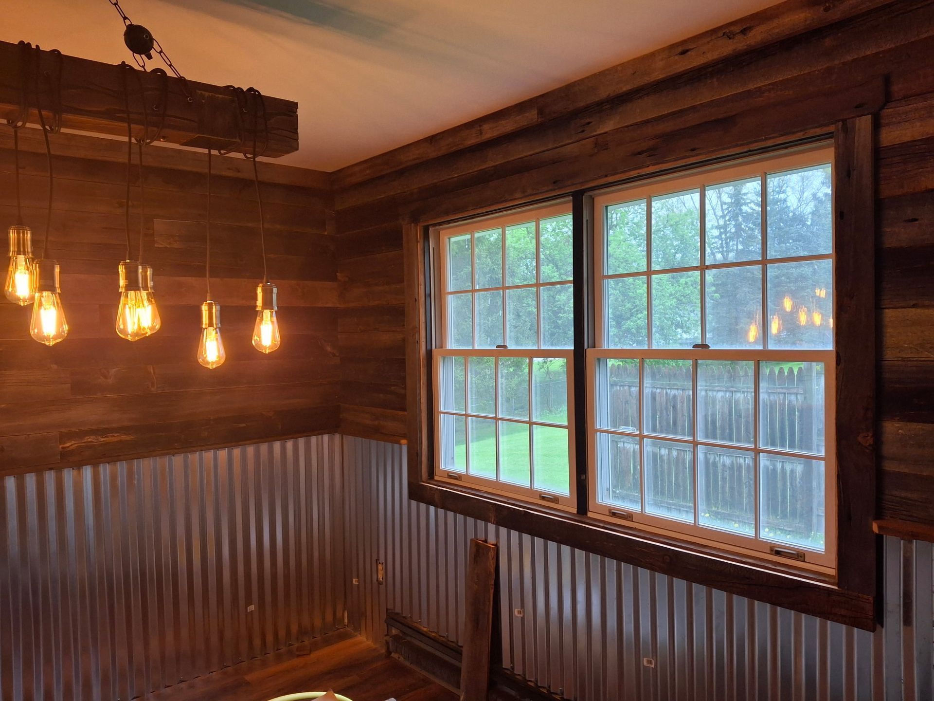 Room with wood and corrugated metal walls, two windows, and hanging light bulbs.
