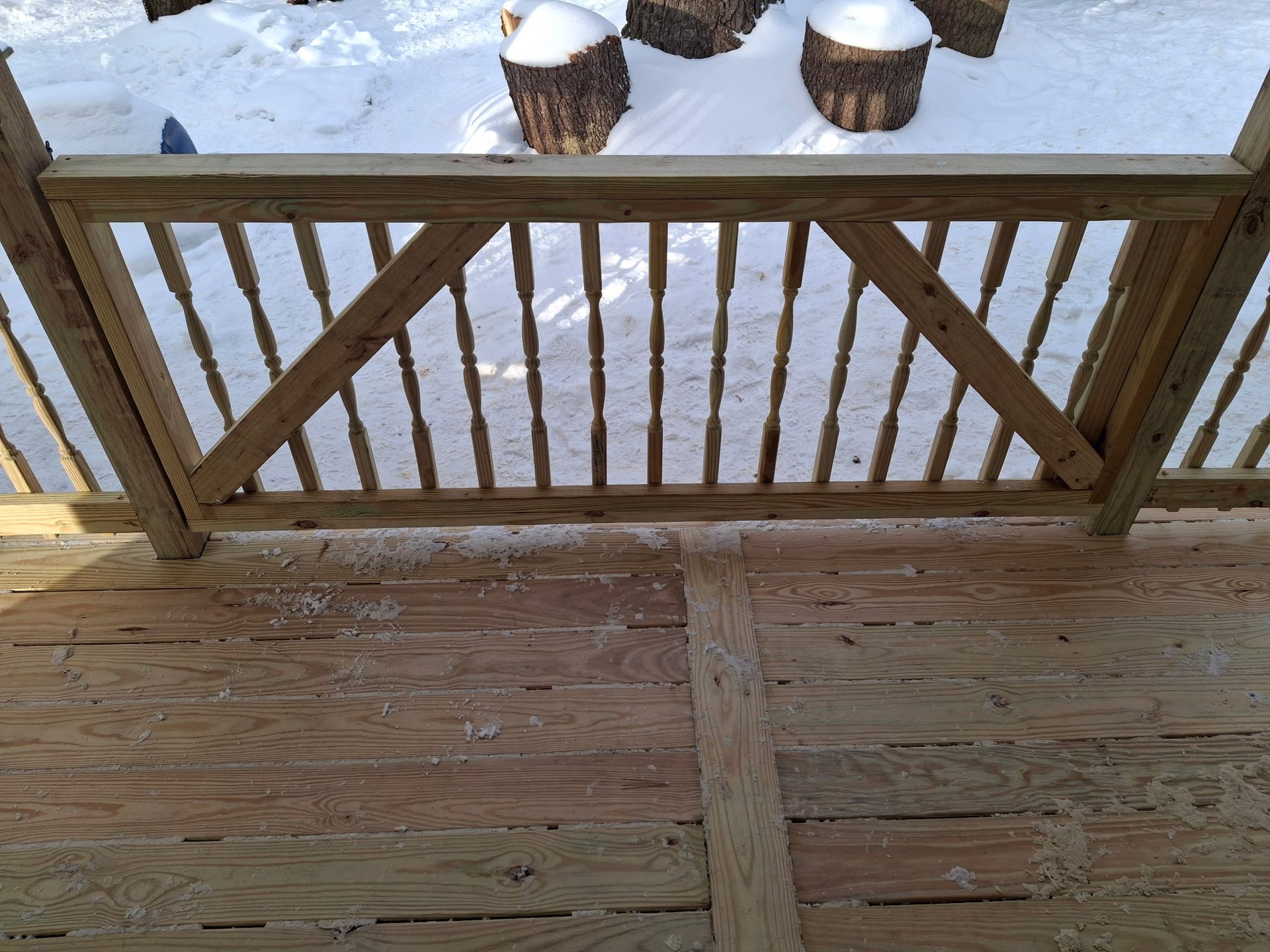 Wooden deck railing on a deck with snow-covered logs in background.