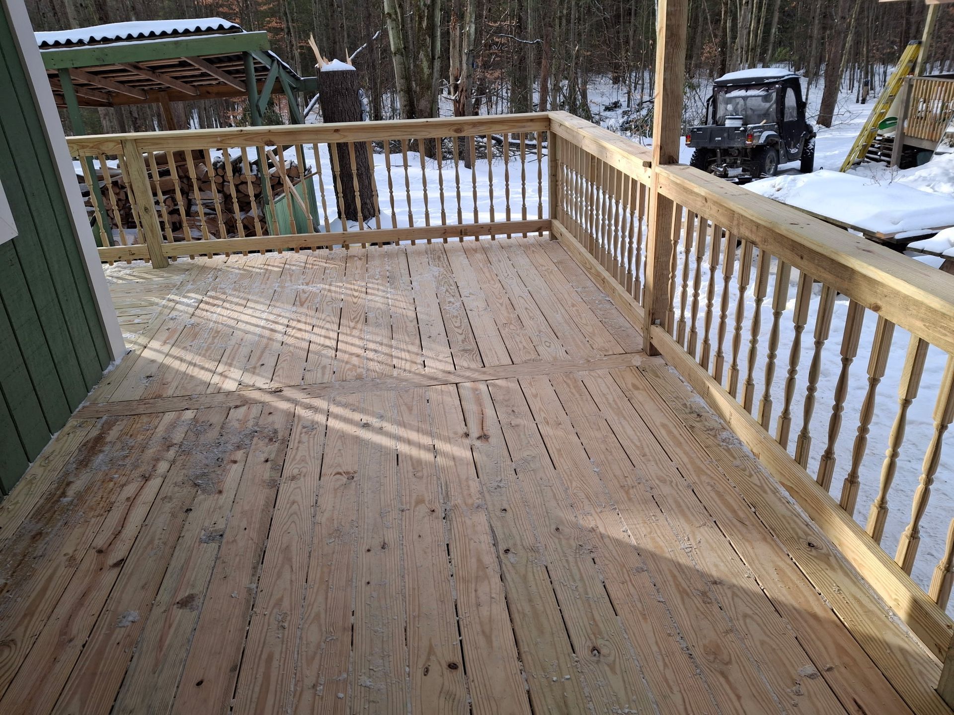 Wooden deck with railing, snow in background. A utility vehicle is parked nearby.