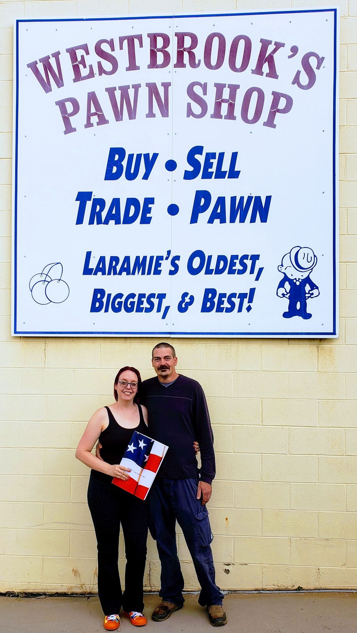 A man and woman standing in front of a sign for westbrook 's pawn shop