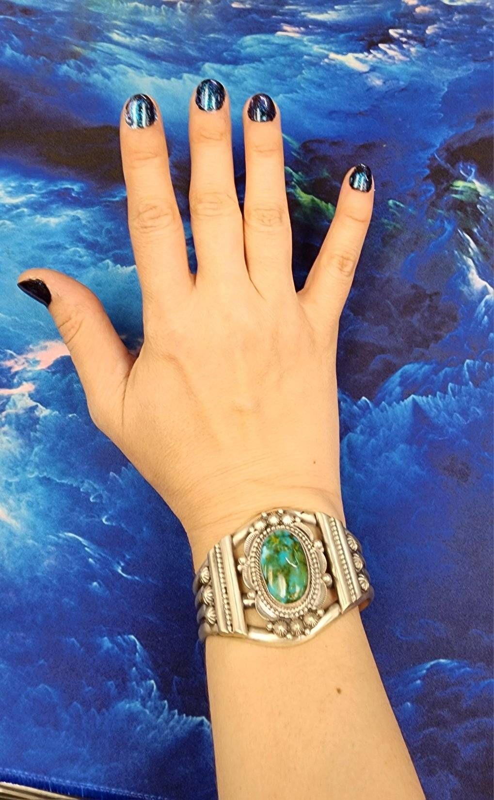 A woman 's hand with black nails and a bracelet on her wrist