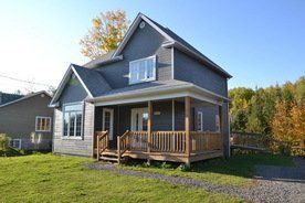 Une petite maison avec un grand porche est située au sommet d'un champ vert luxuriant.