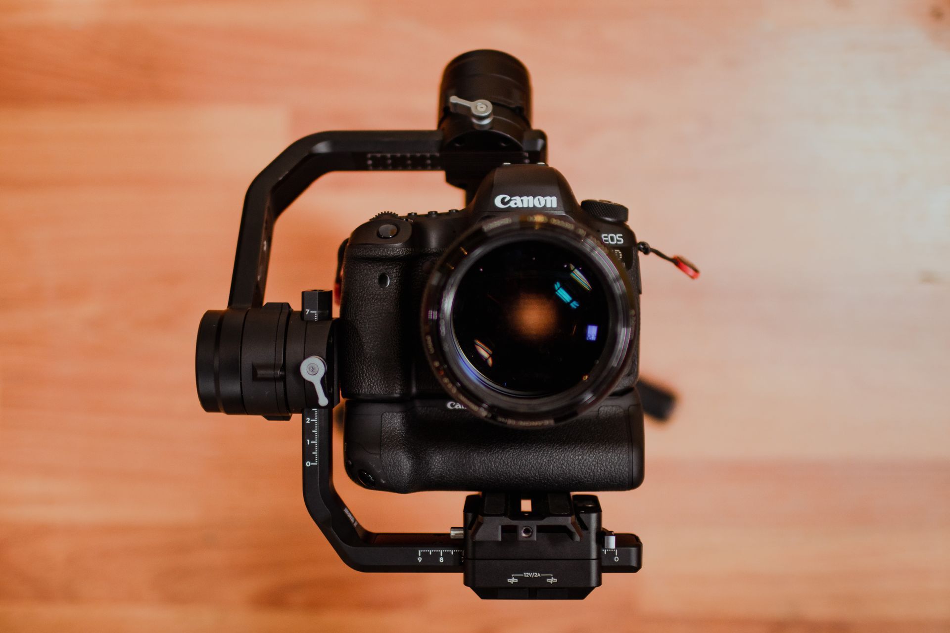 A camera is sitting on top of a gimbal on a wooden floor.