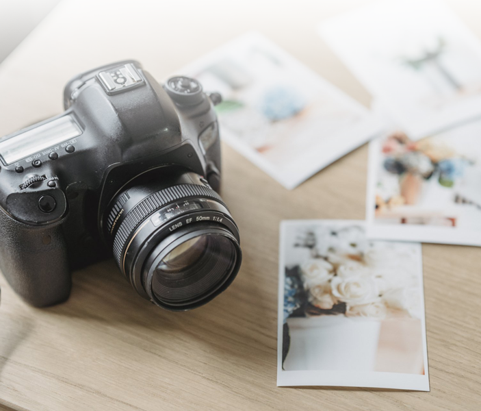 A camera is sitting on a wooden table next to some pictures.