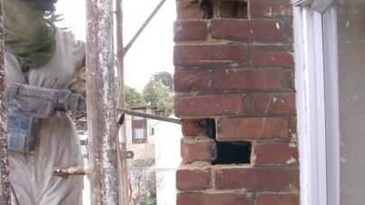 A man is cutting a hole in a brick wall with a hammer.