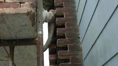 A pipe is hanging from a brick wall next to a house.