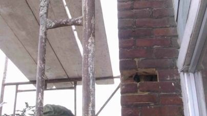 A man is standing on a scaffolding next to a brick wall.