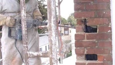A man is using a drill to drill a hole in a brick wall.