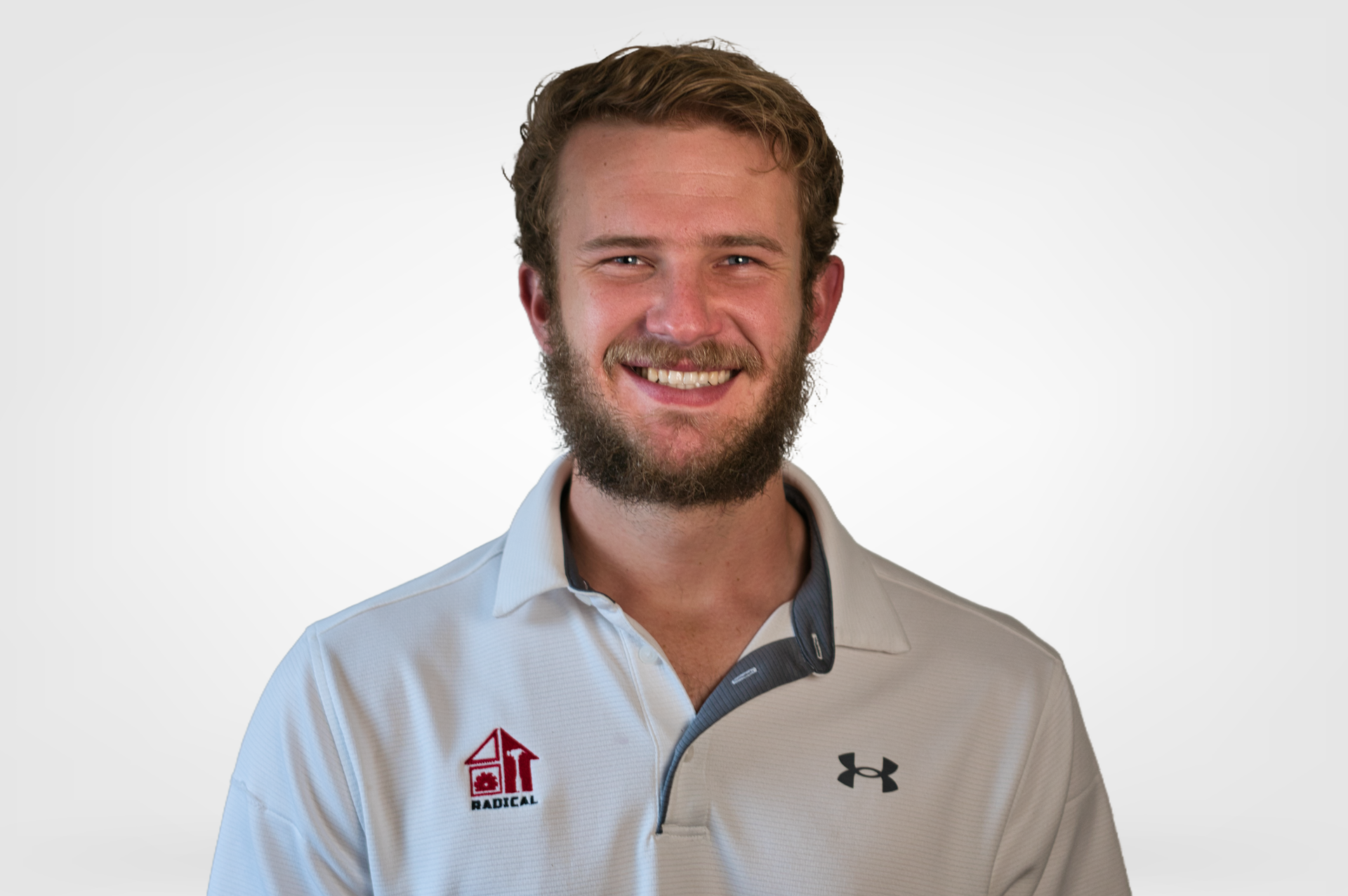 Smiling man with beard wearing a white polo shirt with logo and gray collar.