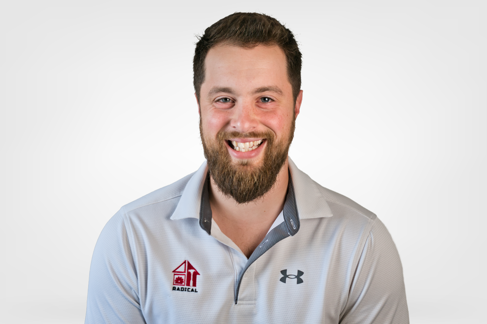 Man with beard, smiling, wearing a light gray polo shirt with a company logo and Under Armour logo.