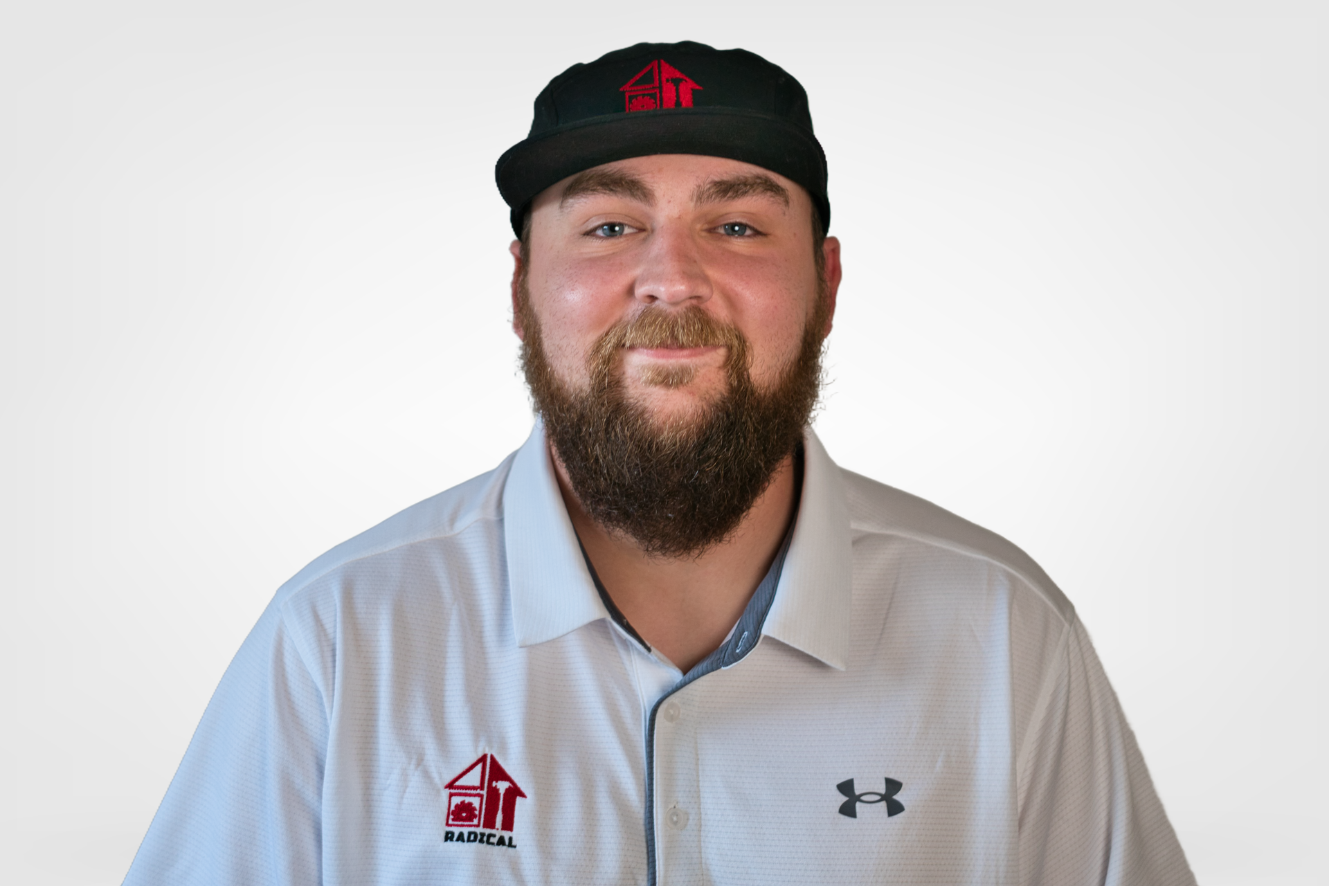 Man with beard and cap, wearing a white shirt with a logo, smiling at the camera.