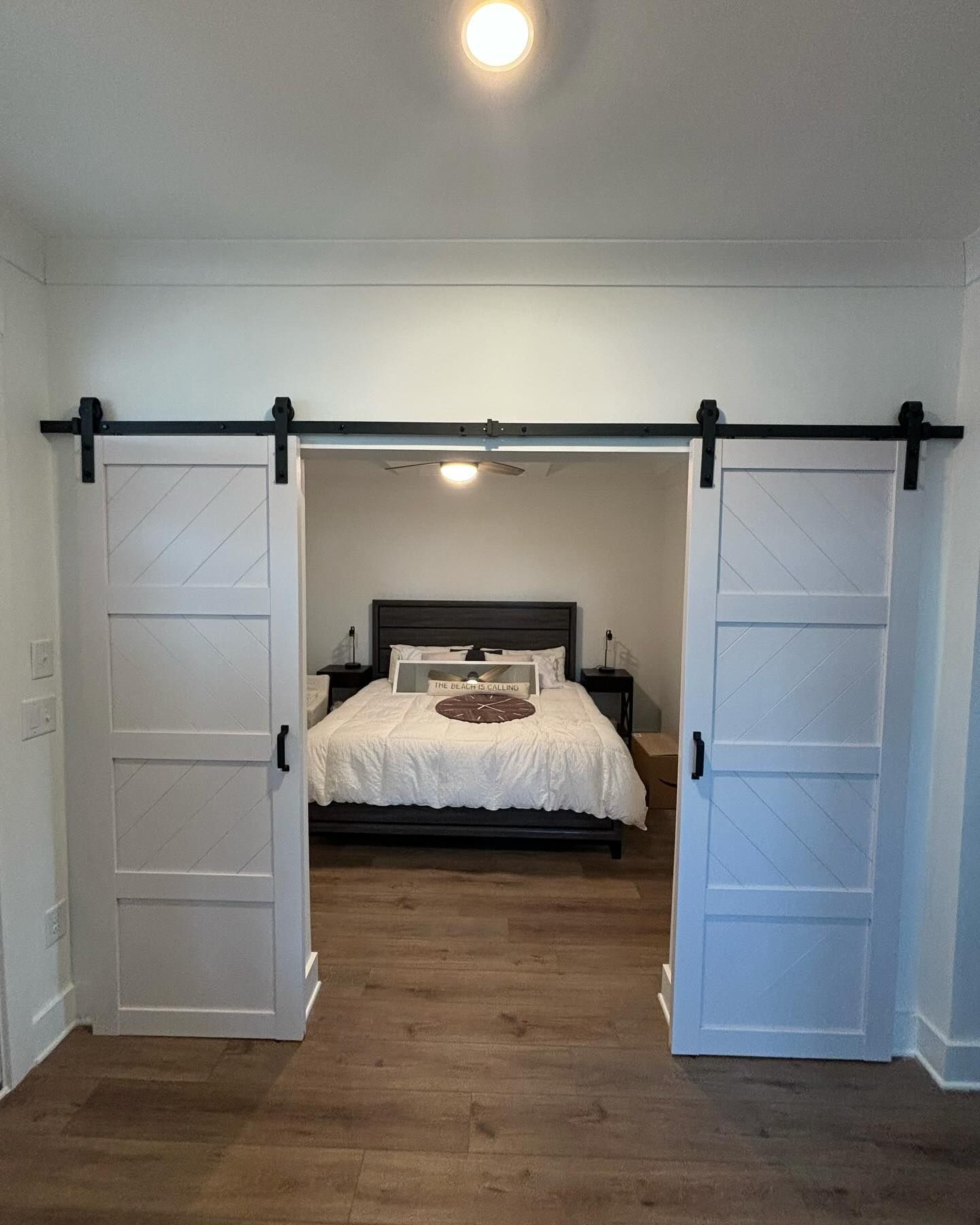 White barn doors open to a bedroom with a bed, nightstands, and a ceiling fan.