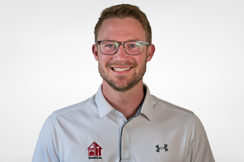 Man with glasses and a gray polo shirt smiles; the shirt has a logo on it.