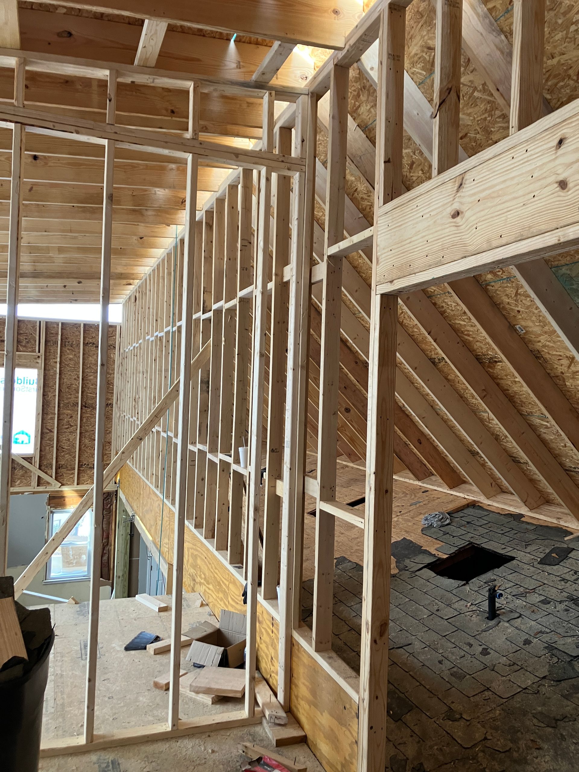 Interior view of a building under construction, showing wooden framing for walls, ceiling, and an open stairway.