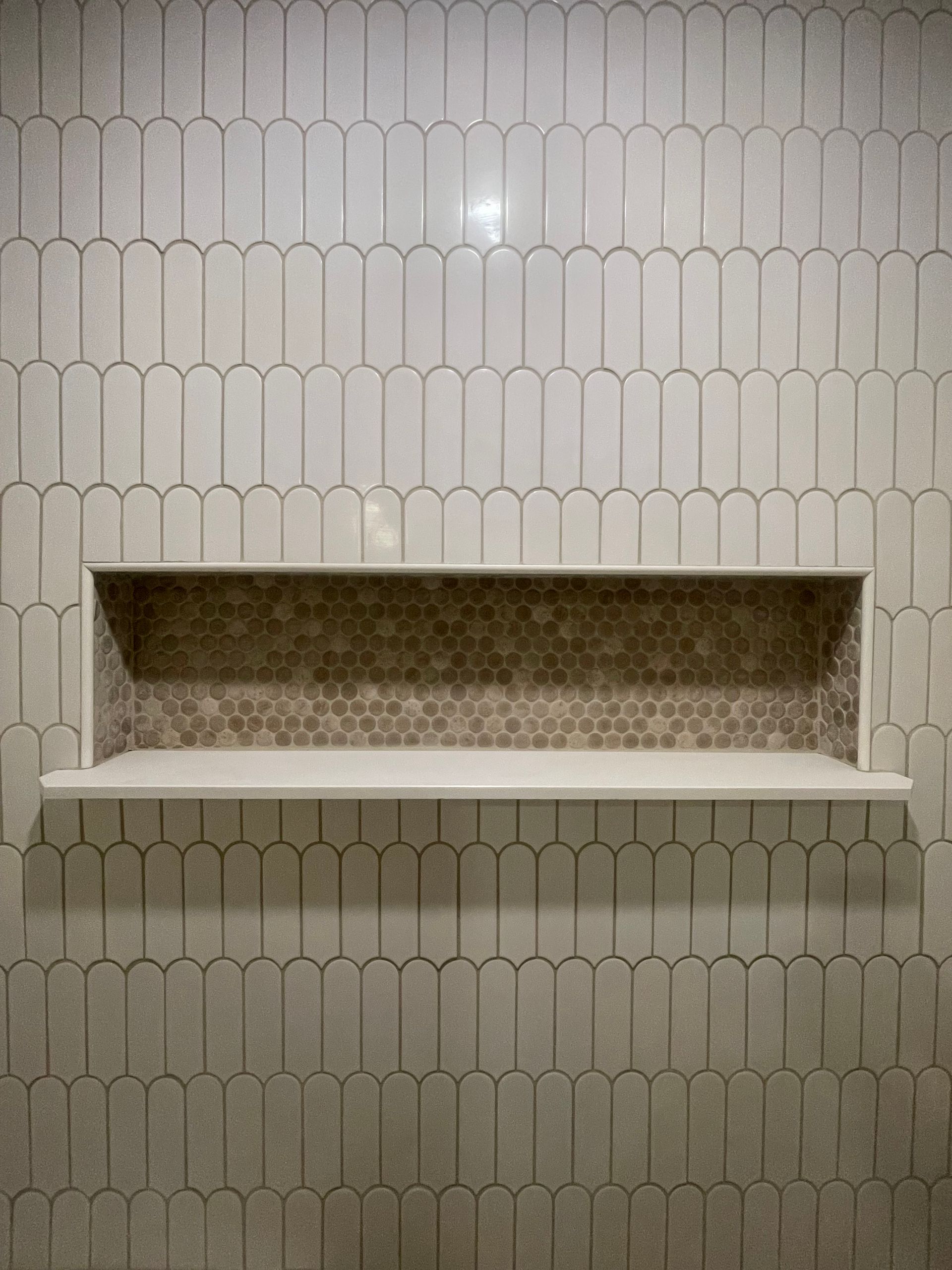 Tile wall with built-in shelf. Long, light-colored tiles frame a recessed niche with brown mosaic tiles.