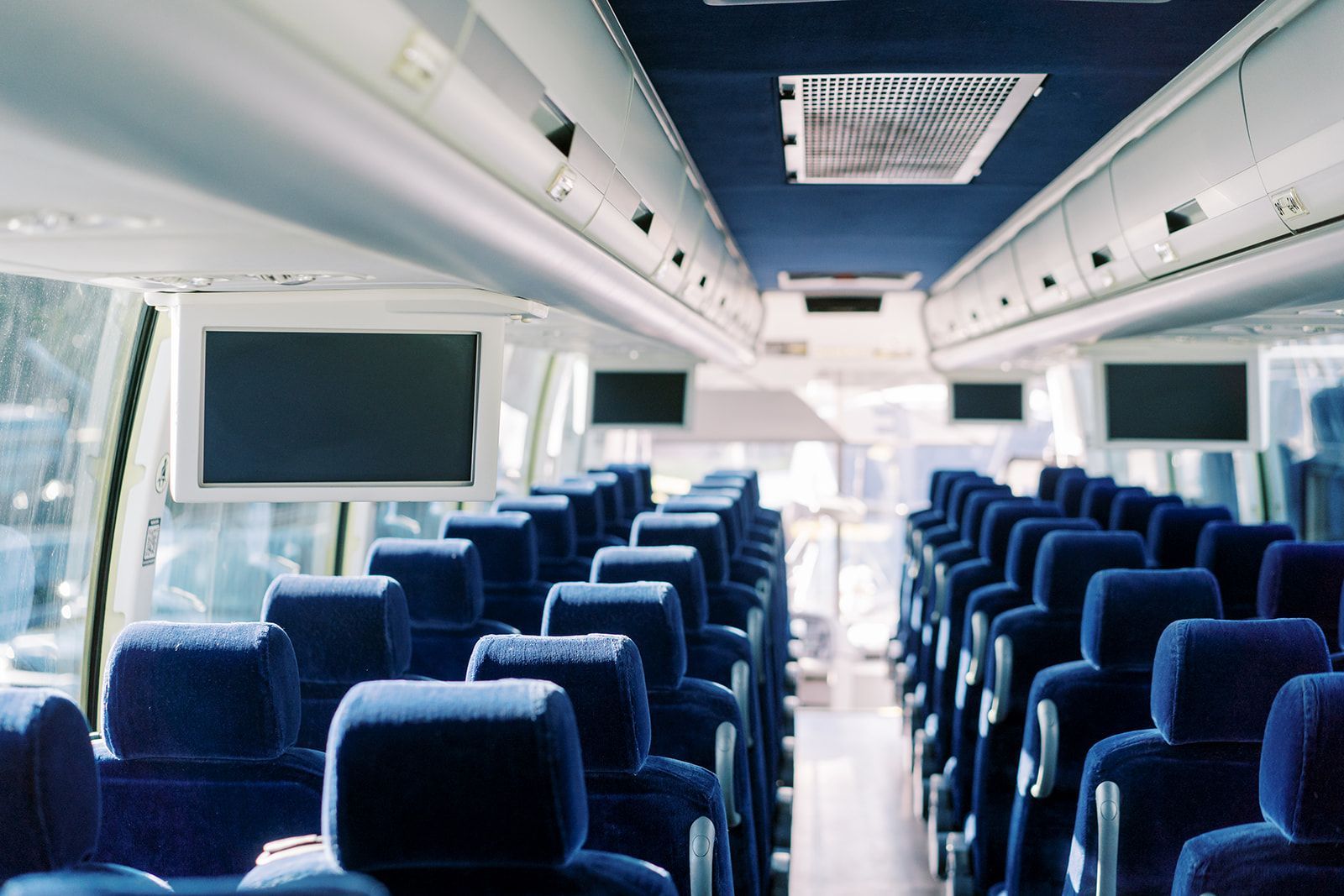 The inside of a bus with blue seats and televisions