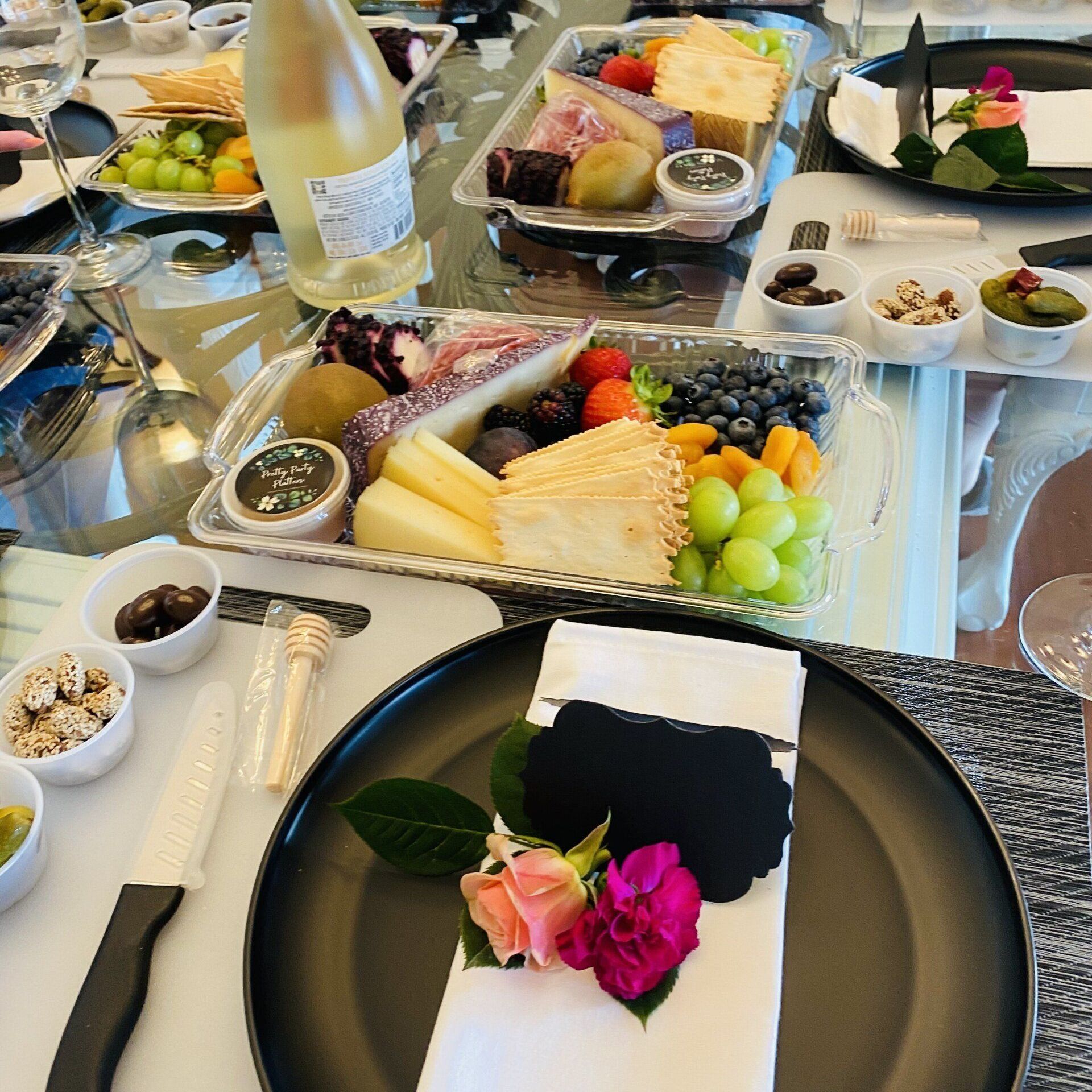 Table set for a party with charcuterie, fruit, wine, and floral napkin rings.