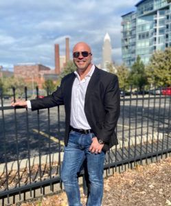 a man in a suit and sunglasses is standing next to a fence .