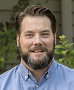 a man with a beard is wearing a blue shirt and smiling