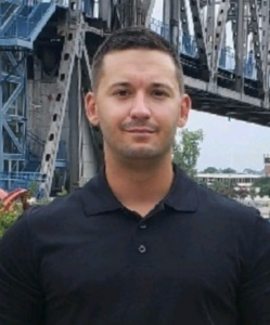 a man in a black shirt is standing in front of a bridge .