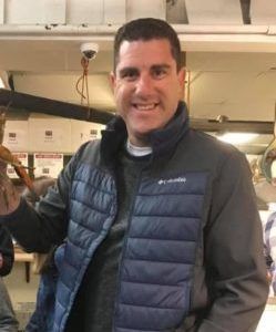 a man in a blue jacket is standing in a room and smiling .