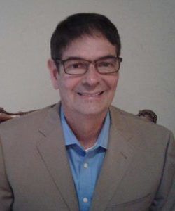 a man wearing glasses and a suit is smiling for the camera .