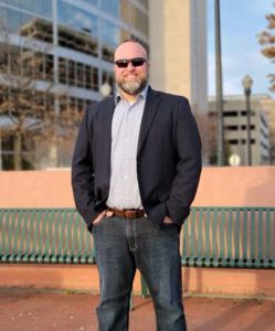 a man in a suit and sunglasses is standing in front of a building .