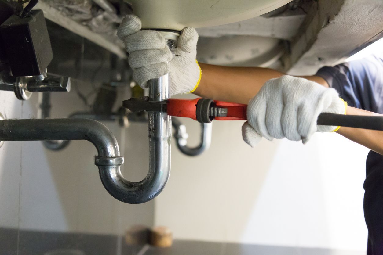 A plumber is fixing a sink pipe with a wrench.